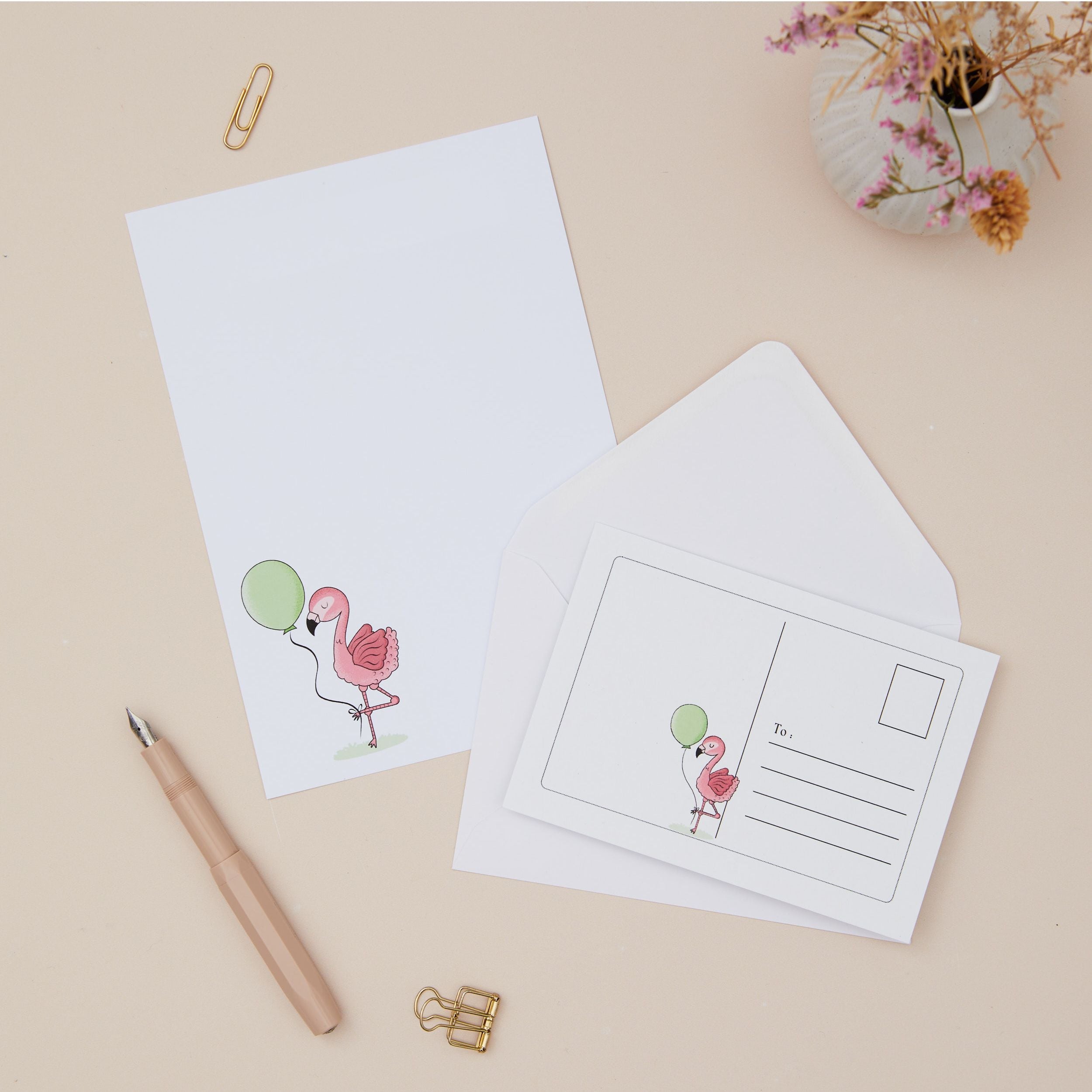 Flamingo Letter Writing Set. Letter Writing Set with Paper, Postcards and Envelopes. The Illustration is a Pink Flamingo holding a balloon. The Stationery set is on a light beige background with stationery and dried flowers.