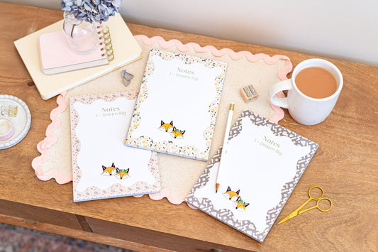 A5 Daily Planners featuring 3 different designs all showing our signature cartoon foxes. Planners are on a wooden desk with a cup of tea.