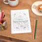 A5 Keep Nurturing Colouring in Notebook, featuring colouring in plants and flowers. The Colouring in Cover notebook sits on a wooden table with pencils, tea and other stationery elements