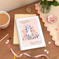 Personalised A5 notebook with a cute cat design and floral elements, set against a pink background, placed on a desk next to a cup of coffee and other stationery items.