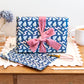 Abstract Blue patterned gift wrapping with a pink bow on a wooden surface with stationery items.