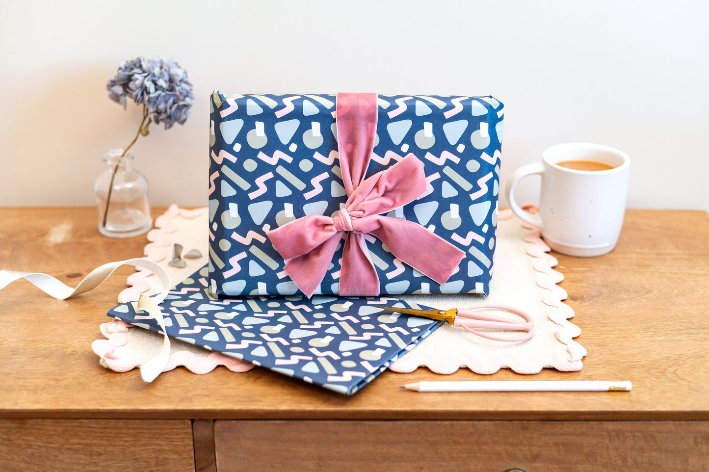 Abstract Blue patterned gift wrapping with a pink bow on a wooden surface with stationery items.