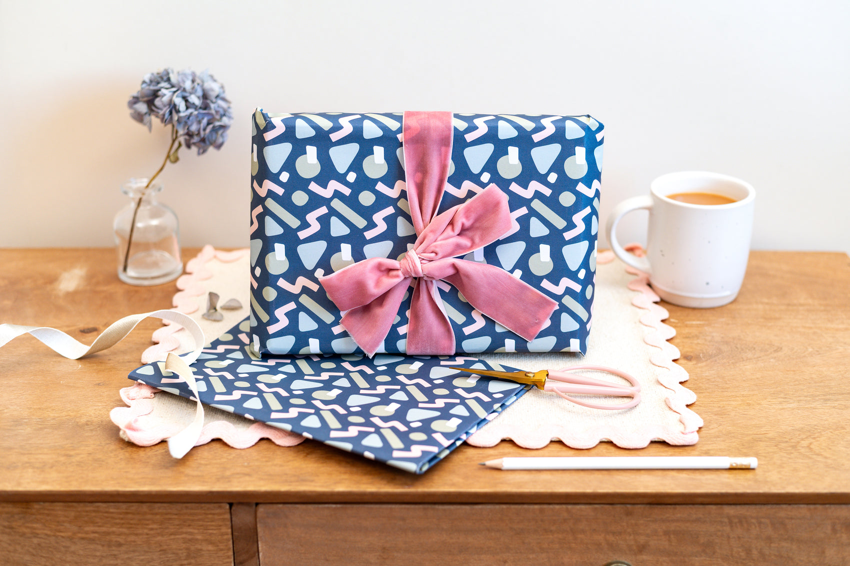 Abstract Blue patterned gift wrapping with a pink bow on a wooden surface with stationery items.