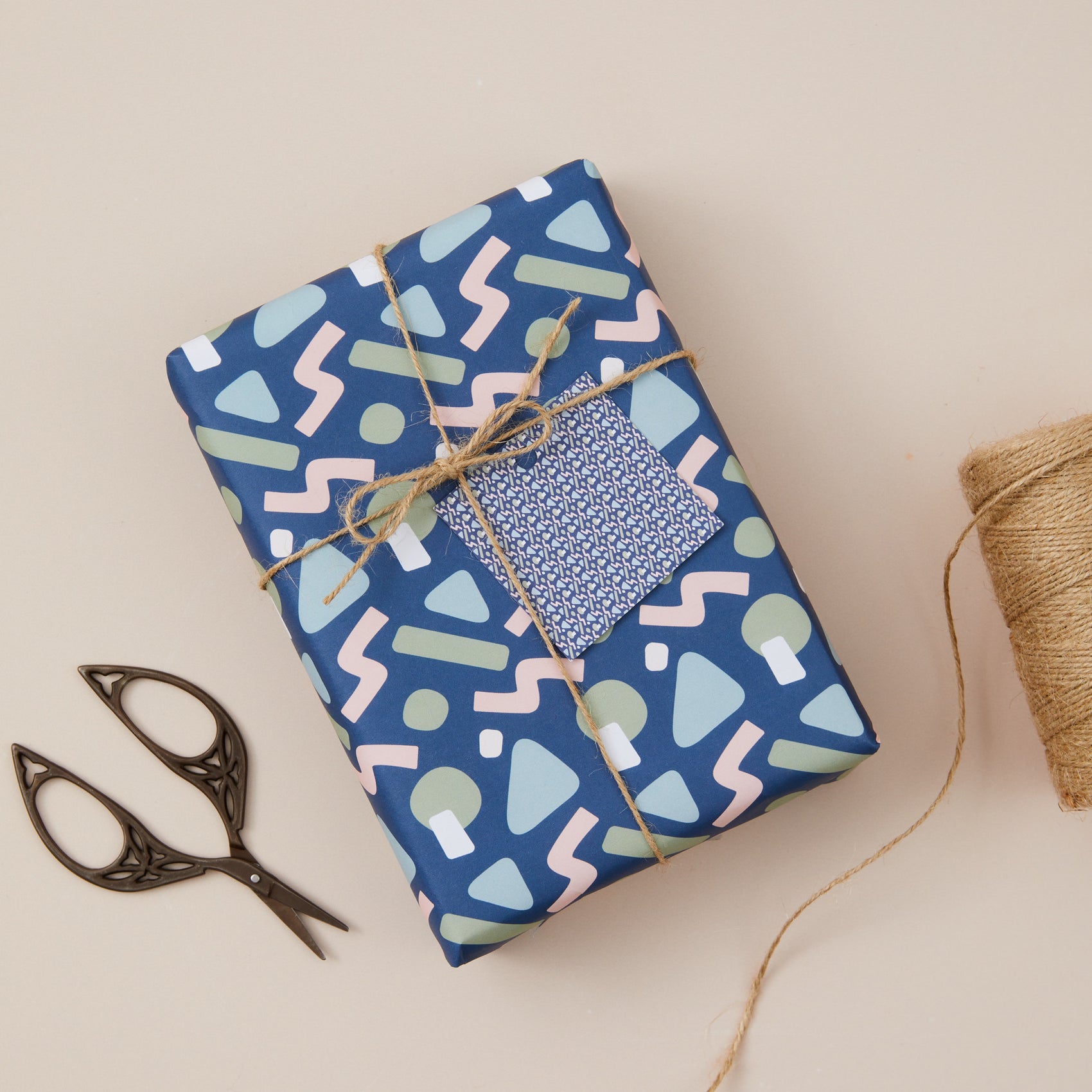 Gift Box covered with Abstract Blue Wrapping Paper and Twine String.  Accompanied by scissors on a beige background