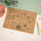 A brown A4 size activity mat with football-themed illustrations, including a soccer ball, cleats, and other sports items, displayed on a table with a green and white checkered napkin, a plate, and some pencils.