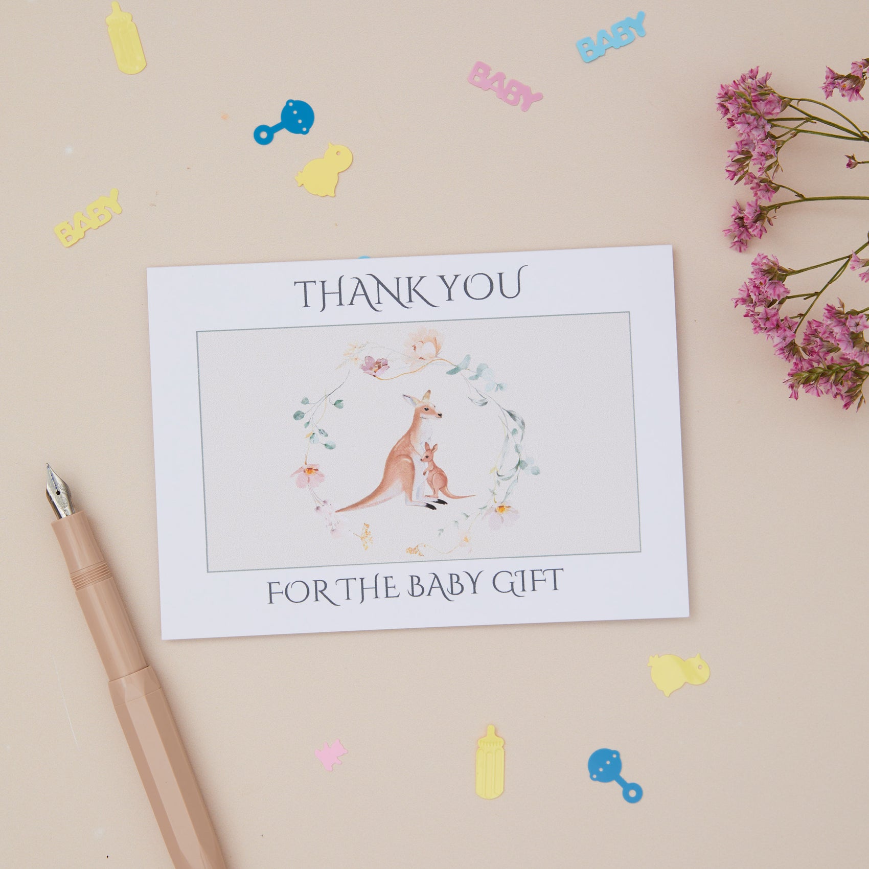 Greeting Card for a Kangaroo and baby set within a floral ring. The card says thank you for the baby gift. The card is set on a neutral background, with stationery elements surrounding it