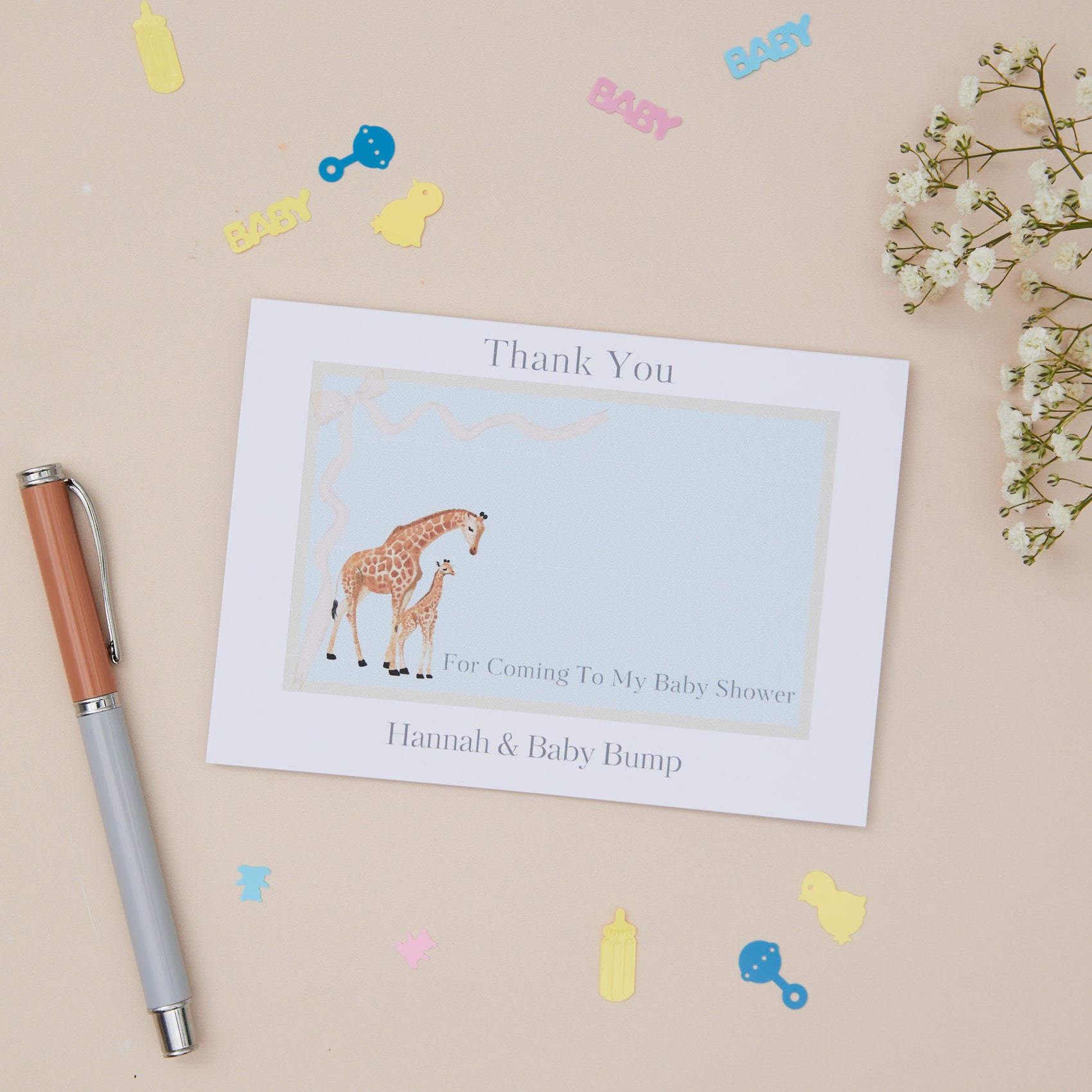 Giraffe and it's young greeting card on a blue background, the card says - thank you for coming to my baby shower - then the mothers name and Bump. The card is set on a neutral background with stationery elements
