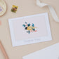 A thank you card with a bird and leaves illustration, placed on a flat surface with a ribbon, stamp, and decorative elements.