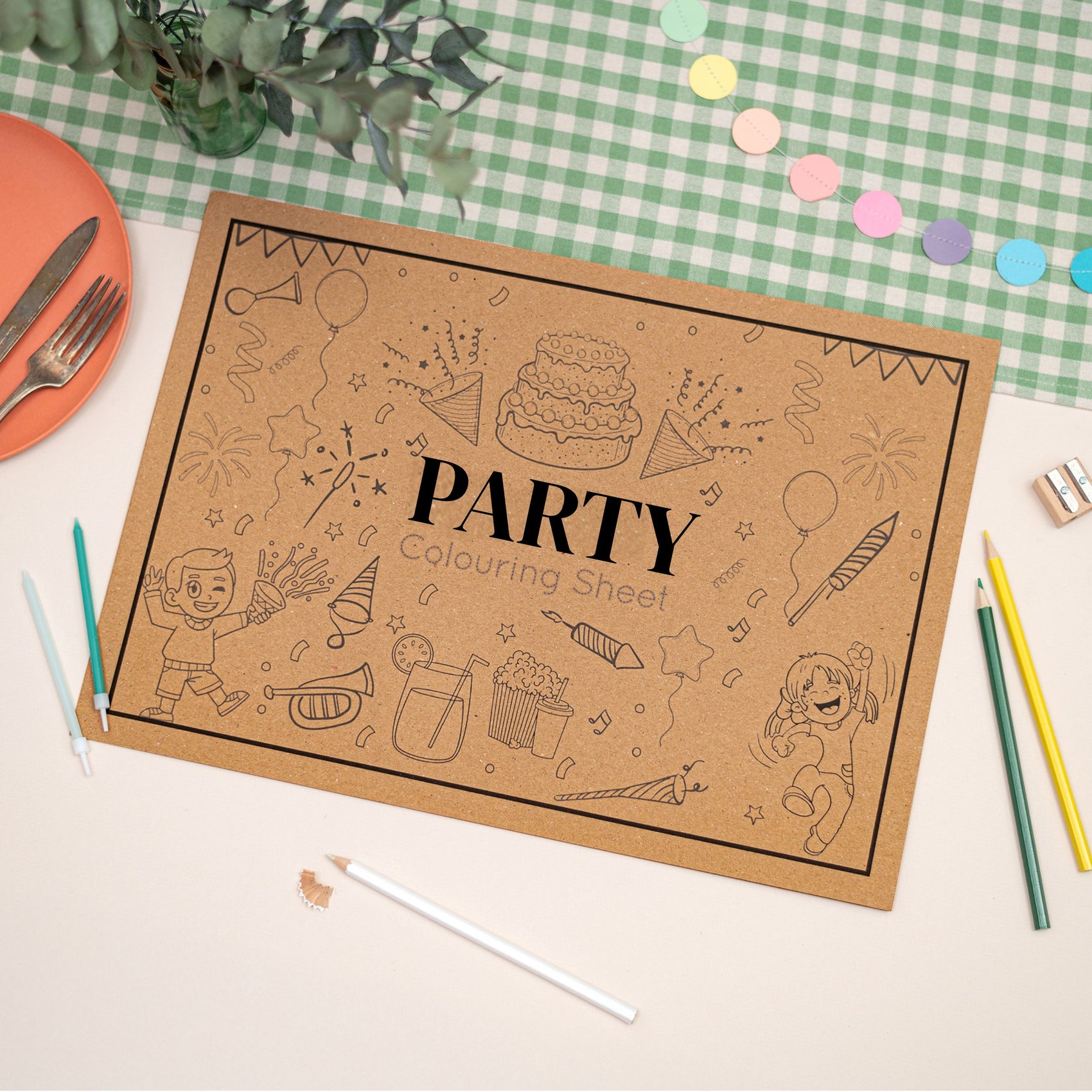 Children's Party-themed colouring Mat. The Mat features a cake, balloons, sparklers and a little boy dancing. The Mat sits on a checkered tablecloth with stationery items.