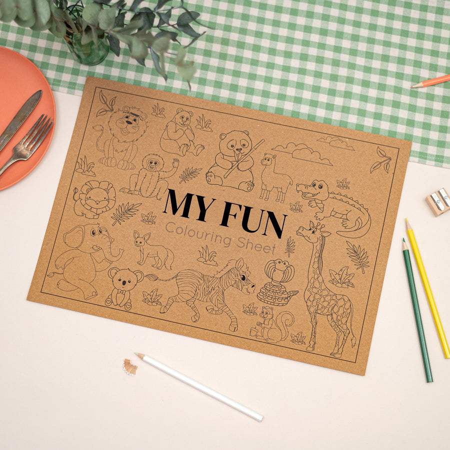 Children's colouring in Coloring placemat. The mat features cartoon jungle animals, and the text "my fun". The Mat is made of Kraft brown paper. The Mat sits on a checkered tablecloth with colouring supplies.