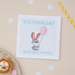 Kids Birthday Greeting card with a cartoon rabbit holding a pink balloon, with the text 'IT'S YOUR DAY HAVE LOTS OF FUN' on a 7x7 inch format, displayed on a neutral background with polka dots and a cupcake.