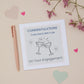 A Dad Engagement Congratulations Card with two celebratory glasses design, accompanied by a pen, and decorative flowers.