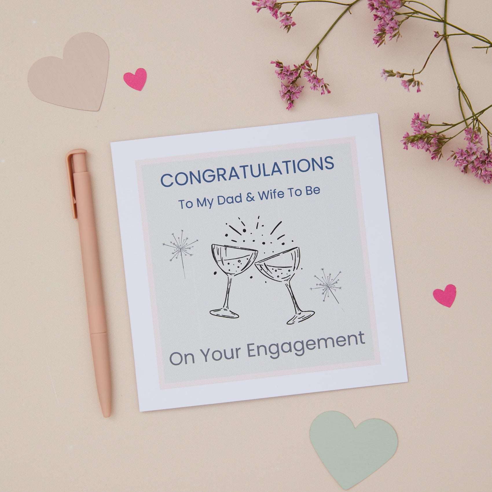 A Dad Engagement Congratulations Card with two celebratory glasses design, accompanied by a pen, and decorative flowers.