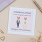 A Daughter Son In Law Wedding Anniversary Card with an illustration of a fox couple dressed in wedding attire, with text that reads 'Congratulations to our Daughter & Son-in-Law, Happy Anniversary'. The card is placed on a neutral background with a white envelope and some decorative elements like a heart clip and dried flowers.