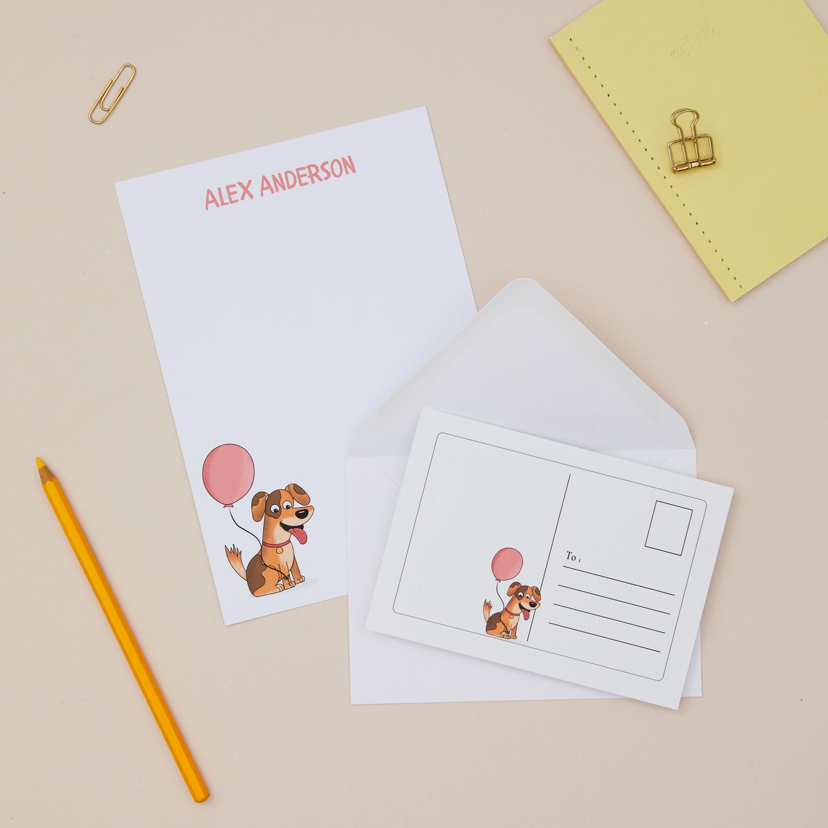 Dog letter writing paper with a dog illustration and pink balloon, featuring the personalised name on a beige background with a pencil and yellow paper clip.