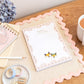 An A5 daily planner pad with a floral and fox design on the cover, placed on a wooden desk next to a cup of tea, a notebook, pens, and scissors.