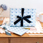 Gift Box wrapped in light blue wrapping paper with scissors & stationery pattern on a wooden table.