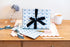 Gift Box wrapped in light blue wrapping paper with scissors & stationery pattern on a wooden table.