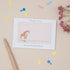 A personalised baby shower thank you card with a cute giraffe and baby design, customised with a name, placed next to a pen, on a background with decorative elements.