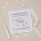 A Granddaughter  engagement congratulations card with two glasses toast design, including two celebratory glasses, accompanied by sparklers. The card is presented on a neutral background, with a decorative ribbon, confetti & pen. The Card features the text " Congratulations to our granddaughter & husband to be - on your engagement.