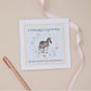 Greeting card with a zebra and its baby illustration within a floral circle on a blue background, and 'Congratulations on becoming grandparents' text. The card is set on a beige background with a ribbon and stationery