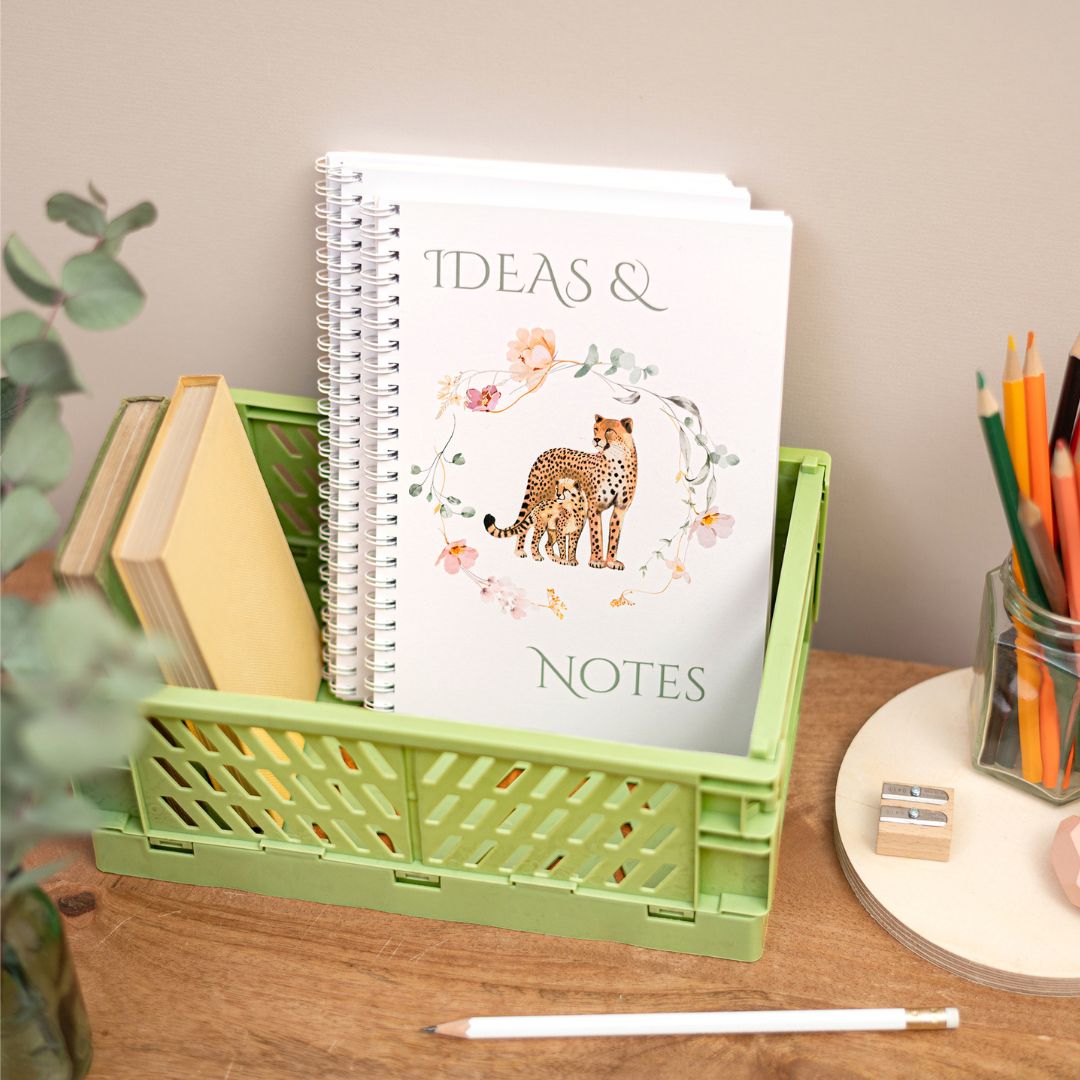 Ideas A5 Wirebound Handmade Notebook. A handmade A5 notebook with a cover featuring a cheetah and baby design, placed on a desk alongside stationery items.
