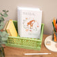Kids A5 Giraffe Notebook. A handmade notebook with a giraffe design on the cover, titled 'Ideas & Notes', placed inside a green basket on a desk alongside books, pencils, and a notepad.