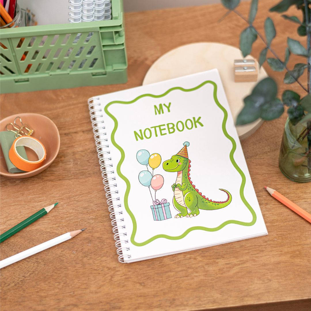 A Kids handmade A5 notebook with a spiral binding at the side. The cover features an illustration of a green dinosaur with birthday balloons and presents.