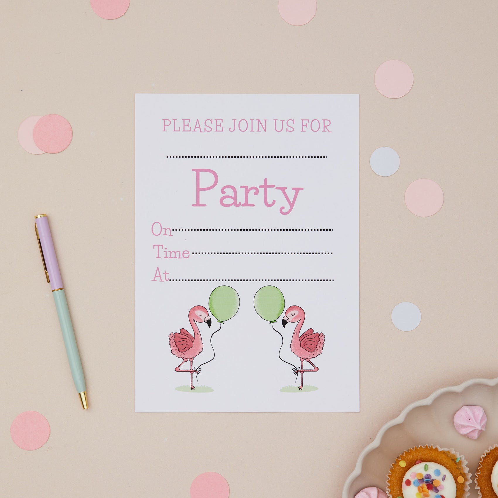 A children's birthday party invitation featuring two pink flamingos with balloons on it, placed on a table with confetti and a pen around it.