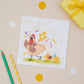 A children's Birthday greeting card with an illustration of a party chicken with chicks, presented on a table with a yellow envelope and decorative elements.