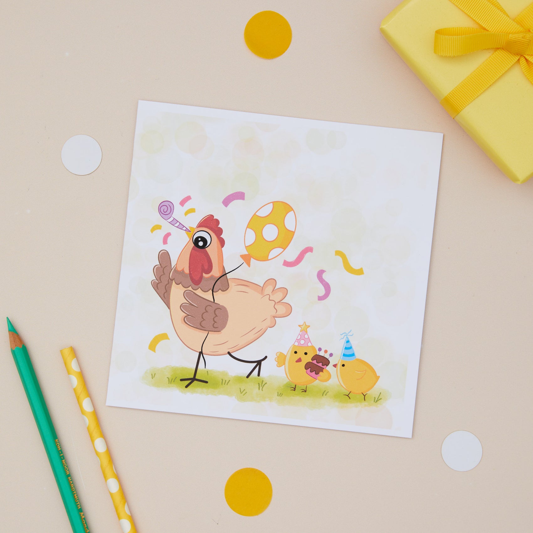 A children's Birthday greeting card with an illustration of a party chicken with chicks, presented on a table with a yellow envelope and decorative elements.