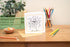 Kids Colouring in Card featuring a party mouse with music notes and party elements around it. The Card is placed on a wooden table with stationery elements surrounding it.