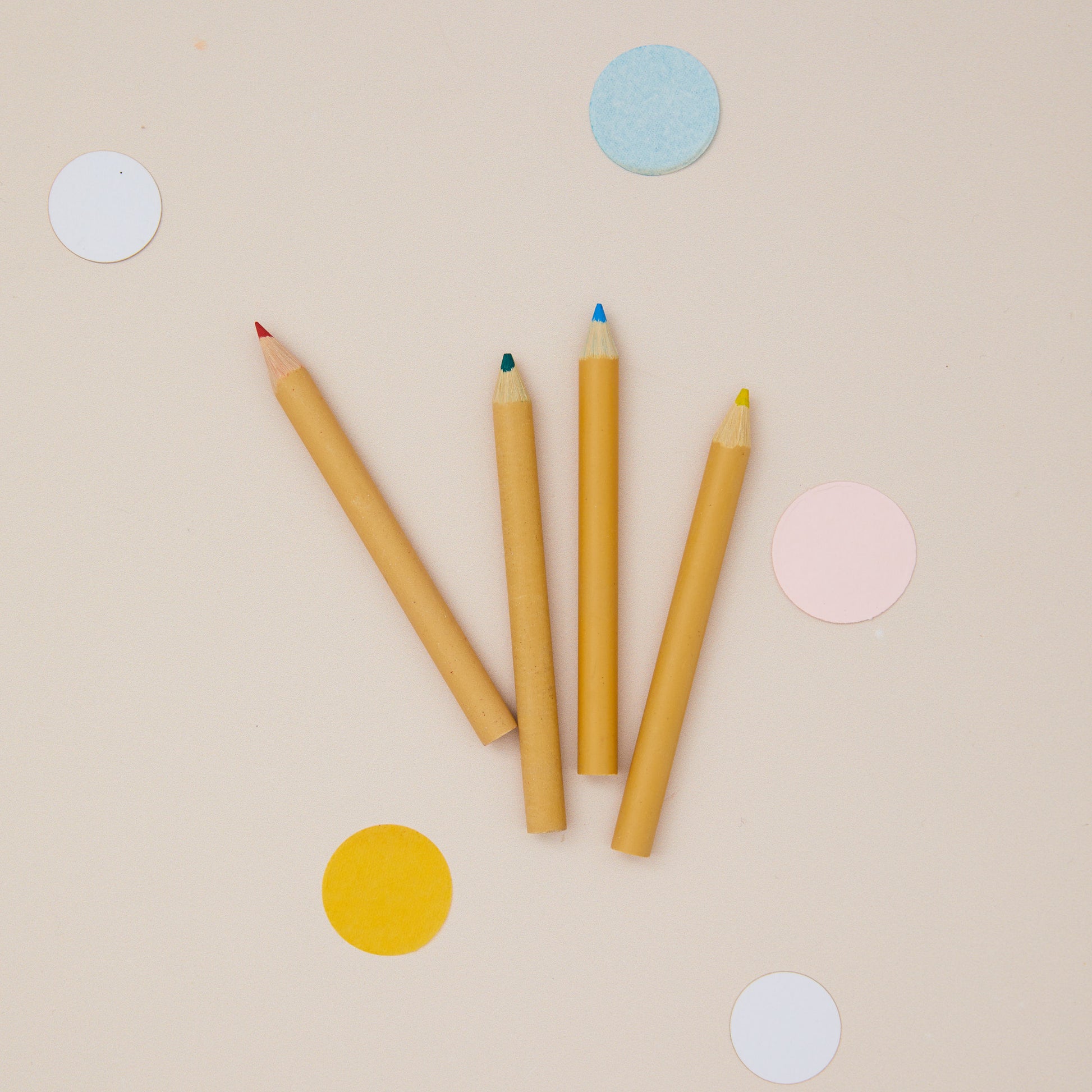Five colored pencils on a beige background with colorful dots.