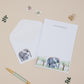 Personalised Letter Writing Set featuring an Elephant and their young within grassy land. Letter Writing Set with matching envelopes, on a beige background.