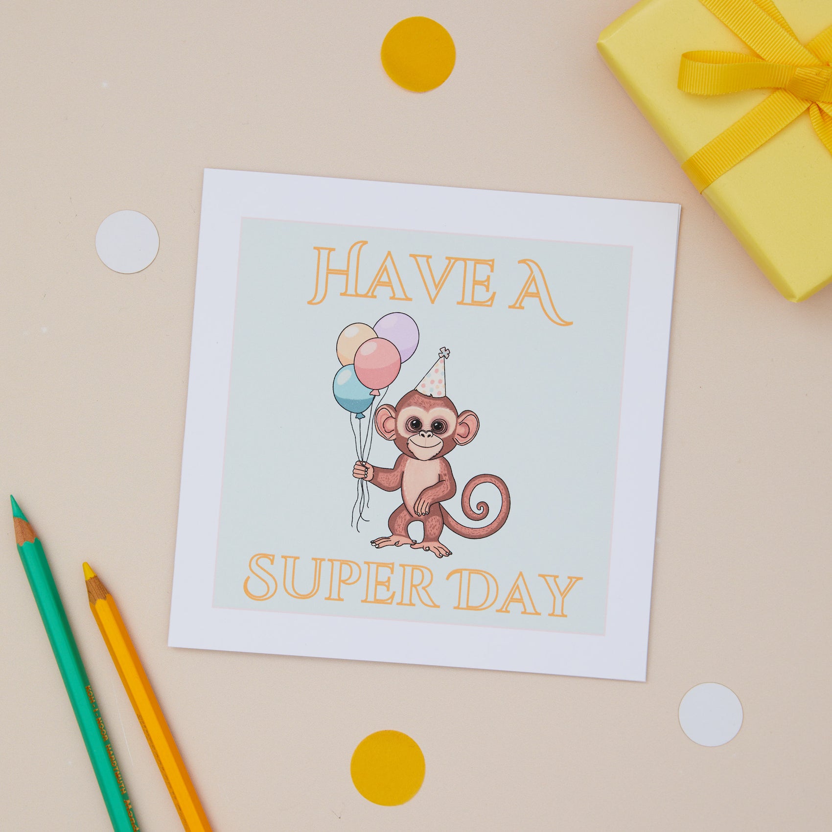 A Kids Birthday greeting card with a cute monkey illustration, balloons, and the text 'HAVE A SUPER DAY' on it, placed on a table with colorful polka dots and a gift in the background.