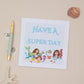 Kids Mermaid Birthday Card with an illustration of mermaids and aquatic life, accompanied by the phrase 'HAVE A SUPER DAY' at the top. The card is displayed on a neutral background with a pen, a shell, and a small decorative butterfly to the side.