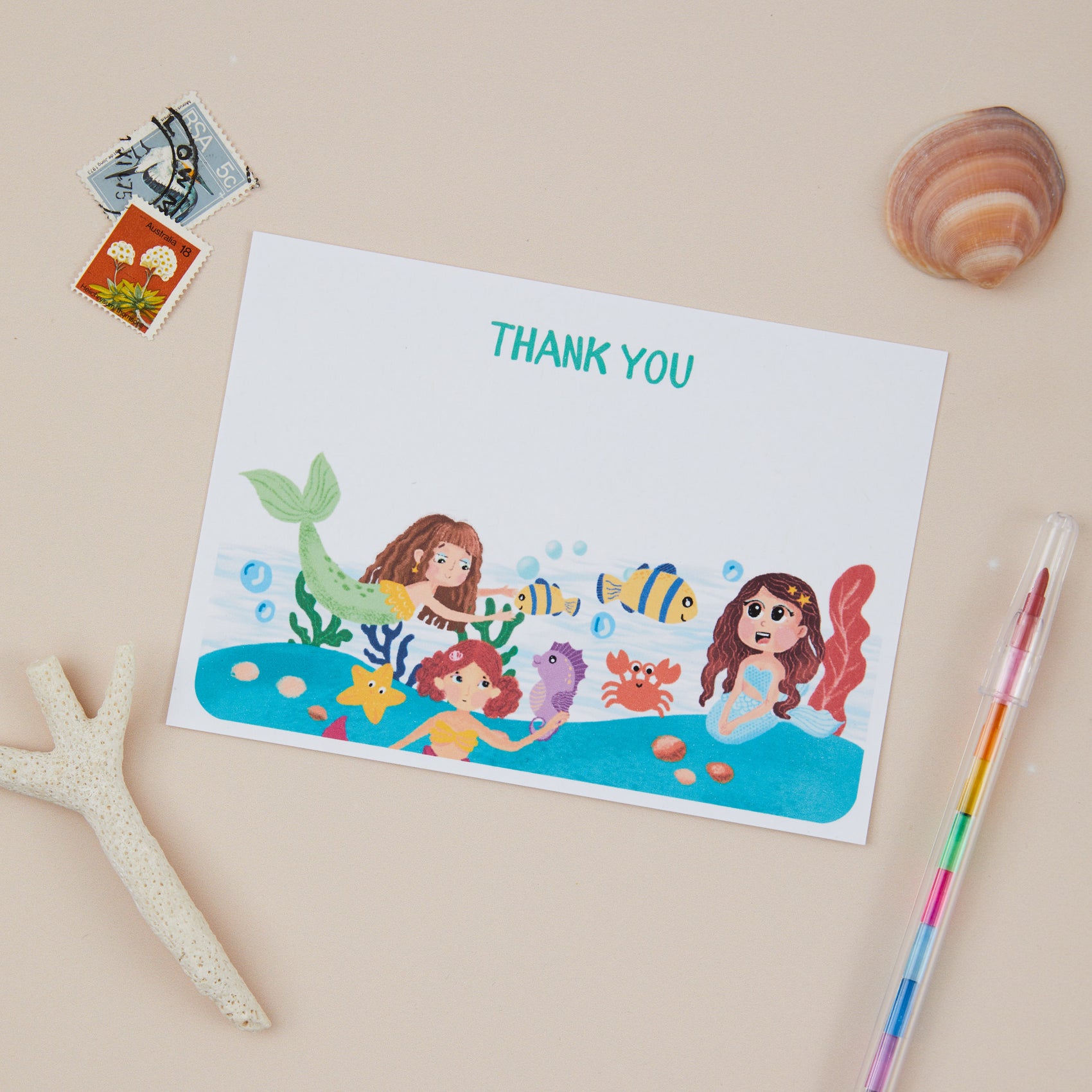 Kids Mermaid Postcard Set. A flat lay  postcard set with mermaid illustrations, accompanied decorative seashells and a starfish on a beige background.