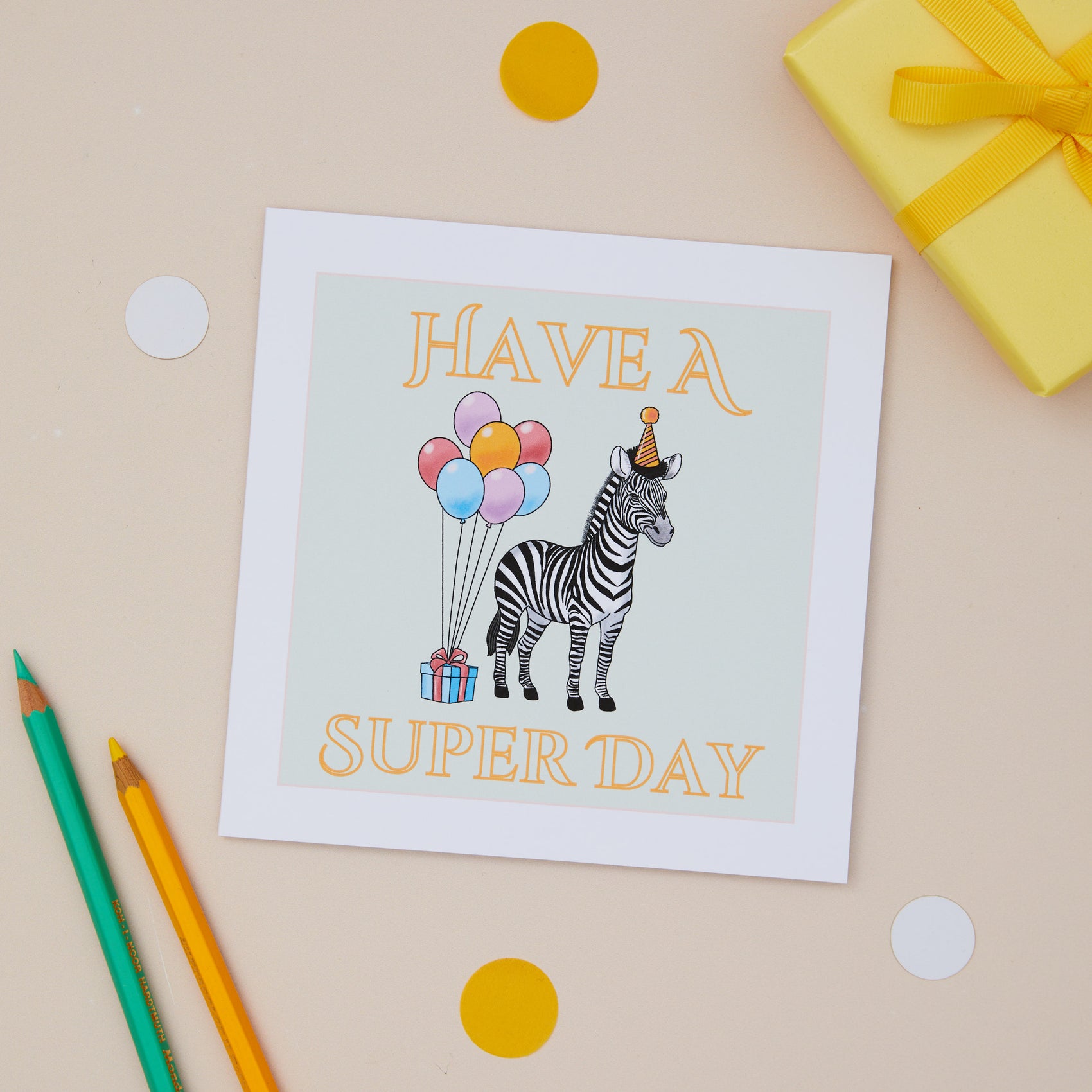 A cheerful children's Birthday greeting card with an illustration of a zebra holding colorful balloons, accompanied by the text 'HAVE A SUPER DAY'. The card is displayed alongside a yellow gift present and colorful decorative elements.