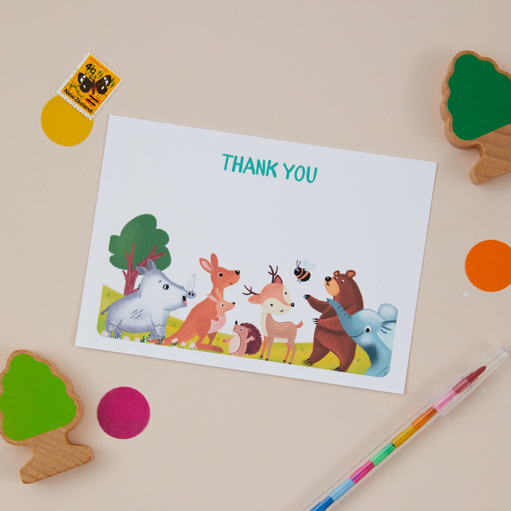 Kids Postcard Set_ Woodland themed featuring illustrations of animals such as a bear, deer, and rabbit, set on a table with colorful circular decorations and a pen.