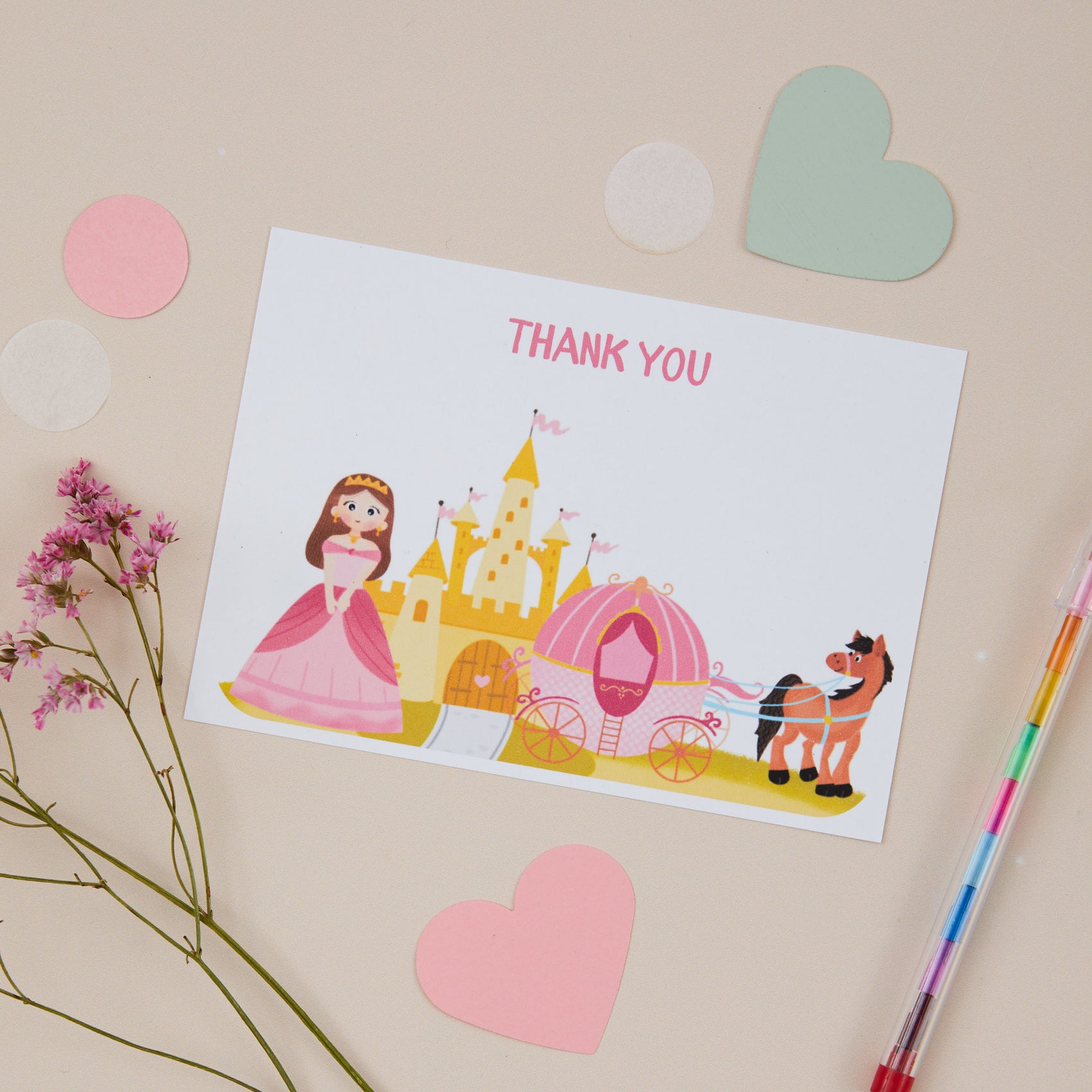 A postcard featuring a princess design with a carriage and horse. In the background there is a pencil and heart-shaped stickers.