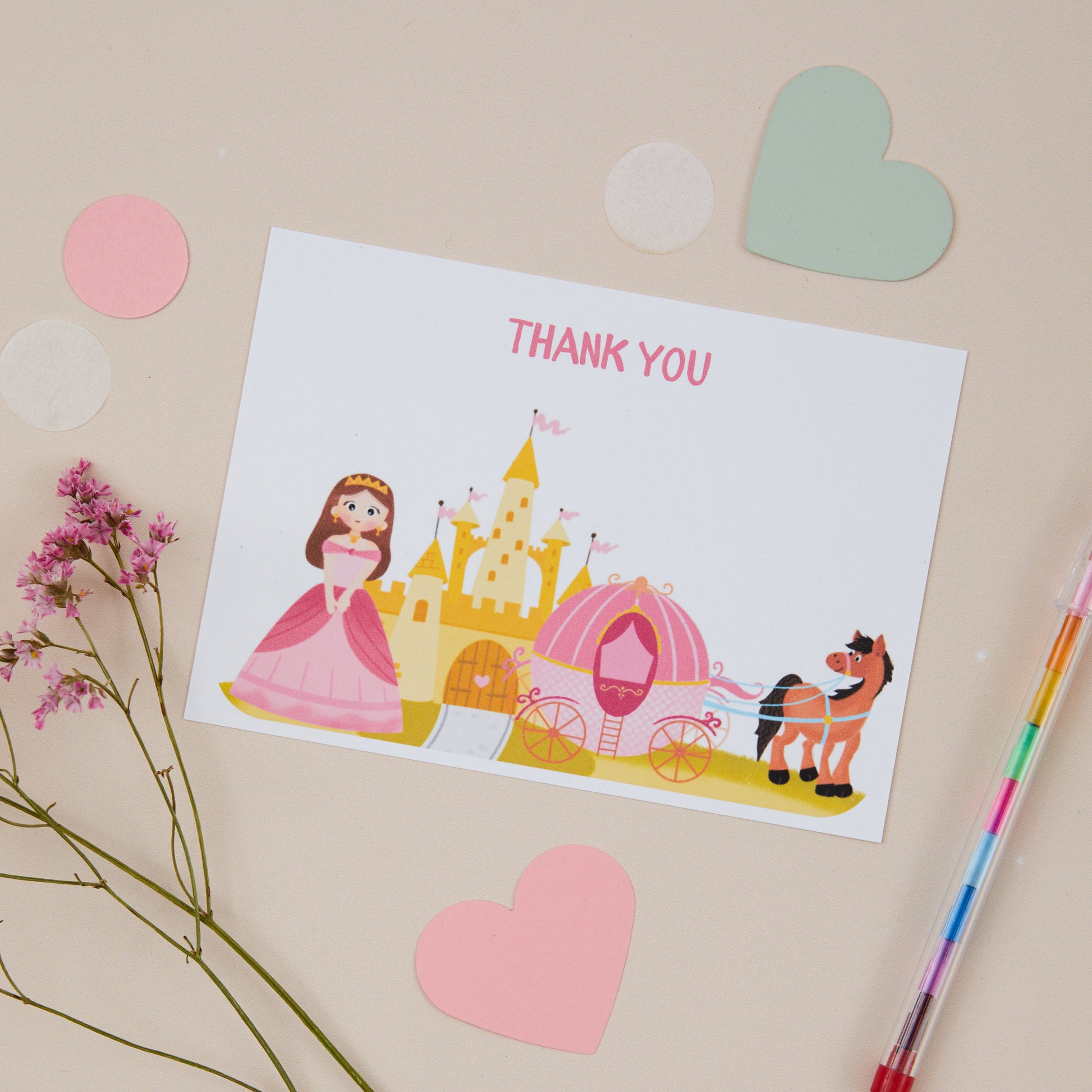 A postcard featuring a princess design with a carriage and horse. In the background there is a pencil and heart-shaped stickers.