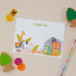 Kids Safari Postcard Set with safari theme illustrations, including a giraffe, zebra, elephant, and lion, alongside stationery and colourful children's drawing supplies.