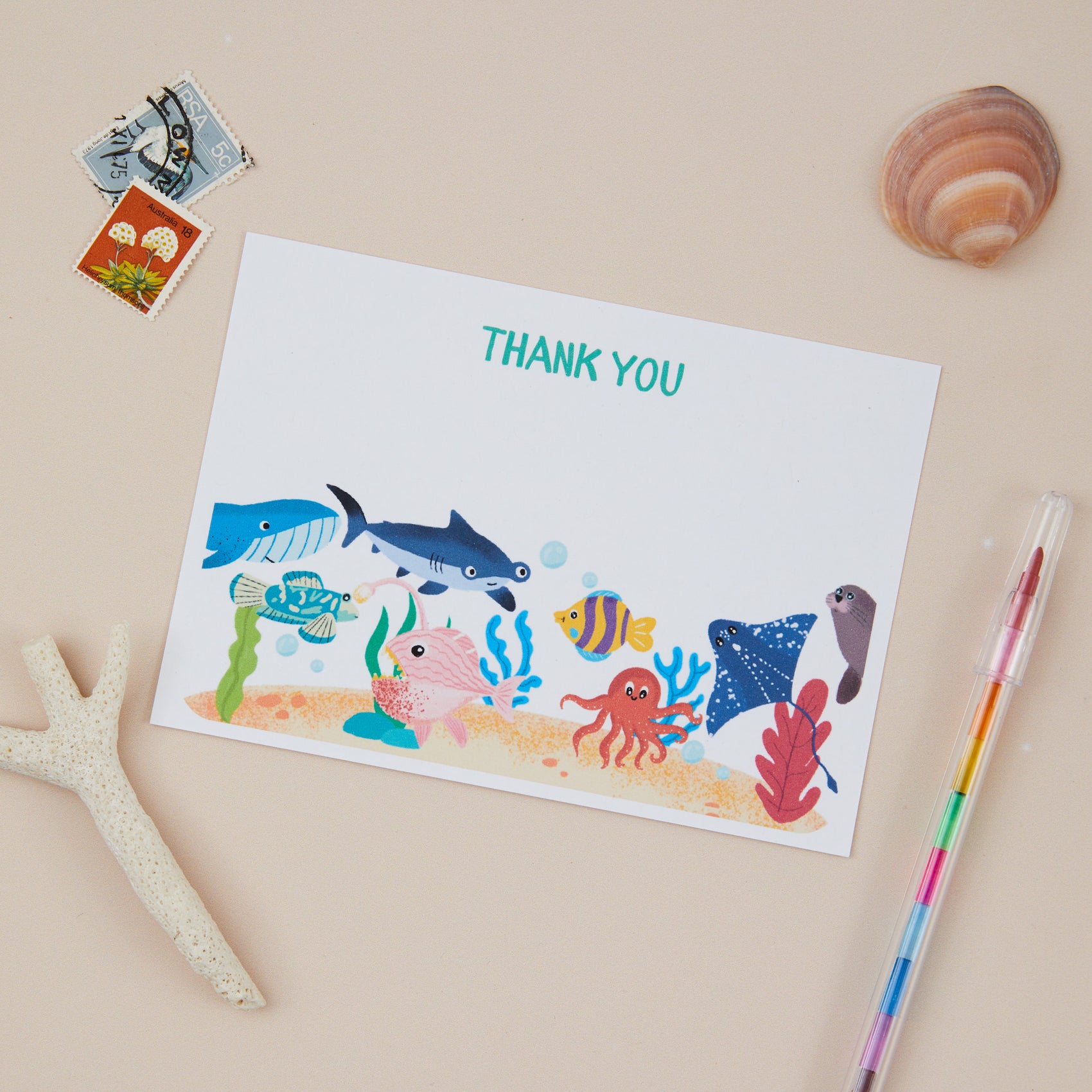 Kids Seaworld Postcard Set. A set of flat thank you postcard set with a seaworld theme, including illustrations of sea creatures like fish and coral, alongside a 'THANK YOU' text at the top. The postcards are displayed with sea elements and a colorful pen on a beige background.