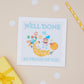 A Kids 'Well Done' card with a cartoon illustration of an astronaut on a star, surrounded by space stars and planets. The Card features the text " well done so proud of you". The card is presented on a background with polka dots.