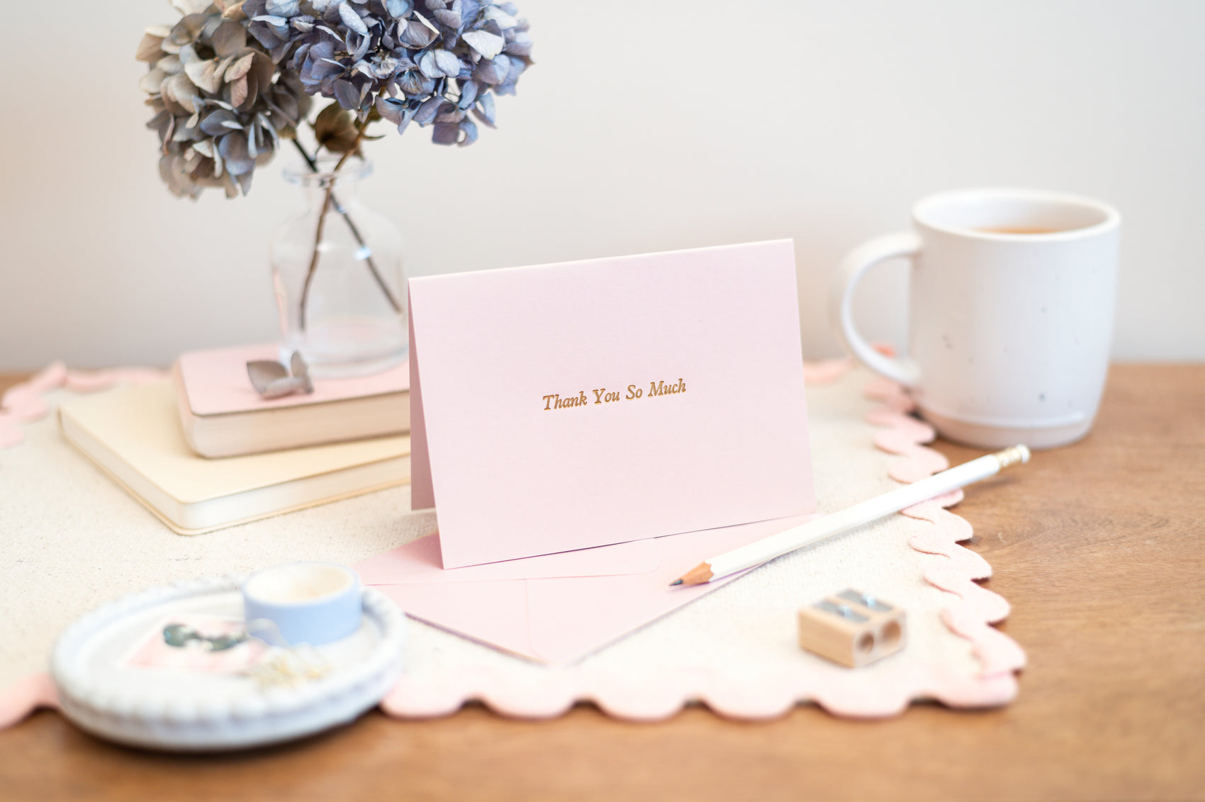 Letterpress Pink Thank You So Much Greeting Card. Pink card with 'Thank You So Much' text on a desk with a mug, books, and flowers.