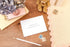 Letterpress congratulations on becoming grandparents card with the words in silver. Card is set against a desk with stationery items