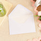 Mockup example of the Luxury Lined White Envelope that will accompany the card.  Envelope is on a table with a pink border table cloth, some tulips, a drink and stationery