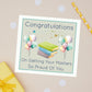 Masters Congratulations Greeting Card with books and balloons on a beige background. The card has the text "congratulations on getting your masters - so proud of you"
