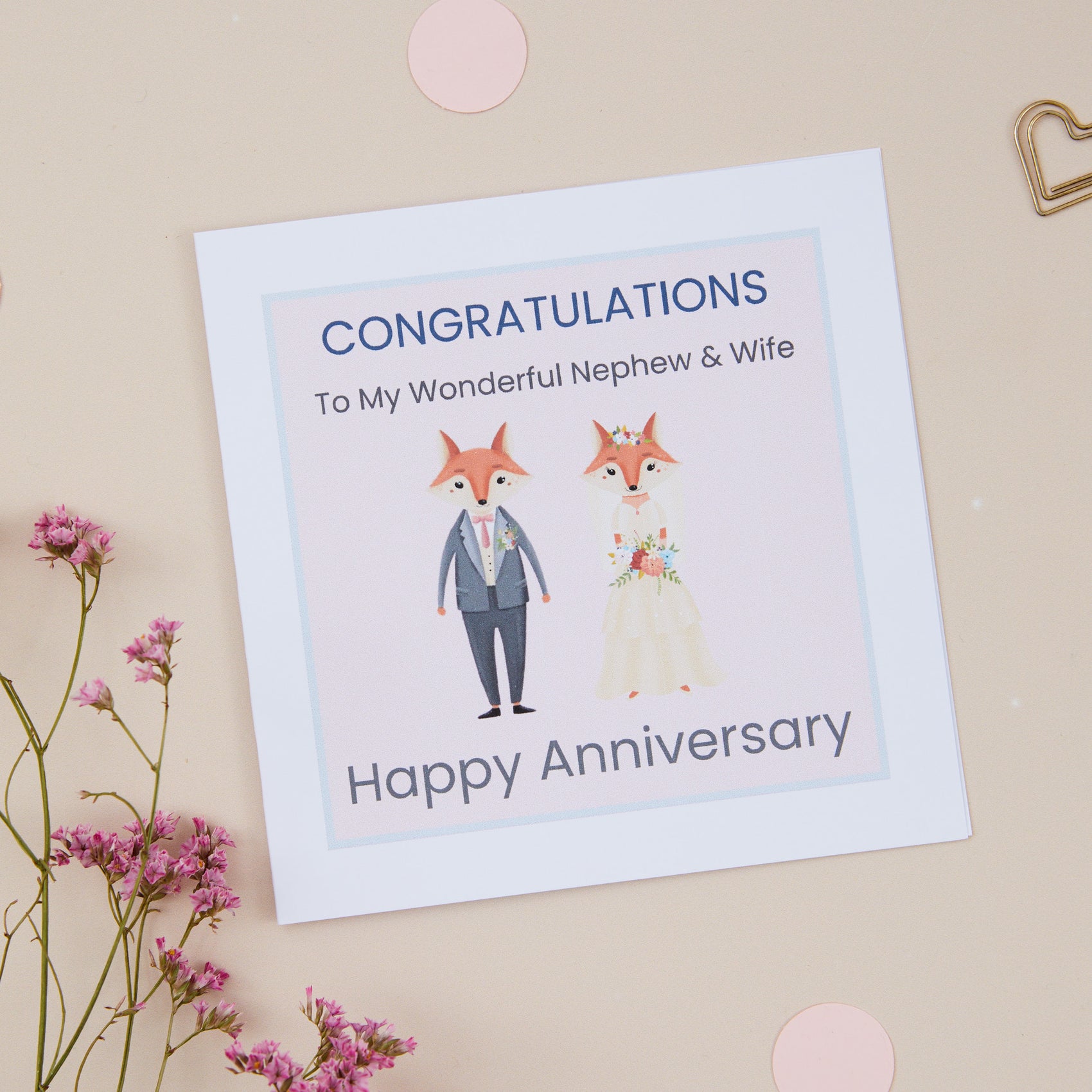 A Nephew Wedding Anniversary Card with an illustration of a fox couple dressed in bridal attire, with the text 'CONGRATULATIONS To My Wonderful Nephew & Wife Happy Anniversary' on it, displayed on a neutral background with some decorative flowers.