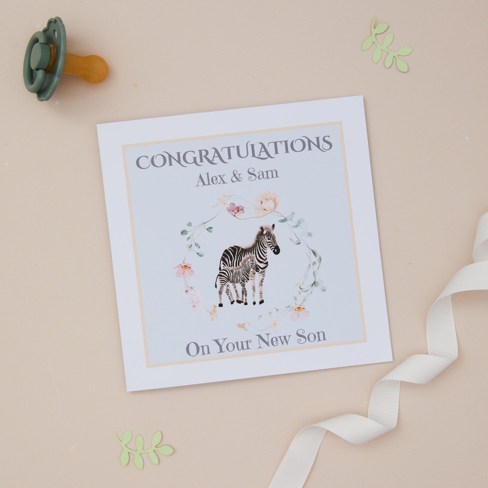 A personalised new baby son card with an illustration of a zebra and its young on a soft blue background, with a yellow border. The card has text congrats on the front and space for a personalized message inside.